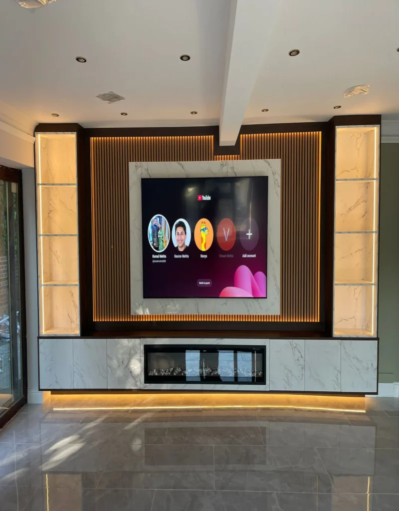 Luxury media wall Sheffield with marble-effect TV surround, backlit slatted panel, built-in electric fireplace, and illuminated display shelving by Xclusive Kitchens